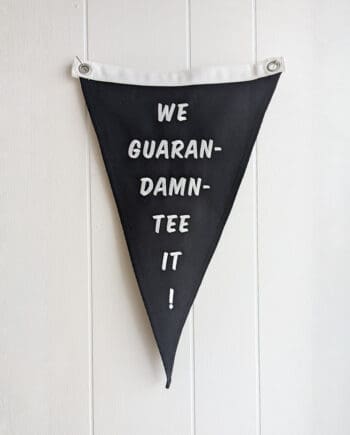 black pennant with two metal grommets embroidered in white with the phrase "we guaran-damn-tee it"