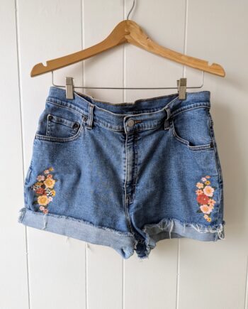 vintage pale blue denim shorts. the right side of the shorts are embroidered with flowers. the lift side is also embroidered with flowers and also a gold tiger moth.