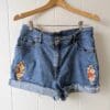 vintage pale blue denim shorts. the right side of the shorts are embroidered with flowers. the lift side is also embroidered with flowers and also a gold tiger moth.