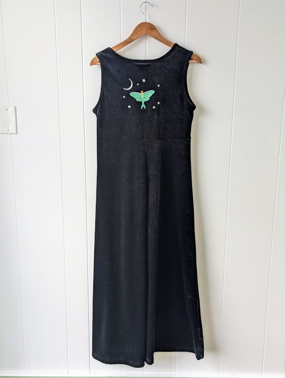 the back of a long black velvet dress embroidered on the top middle back with a luna moth surrounded by a crescent moon and several small stars.