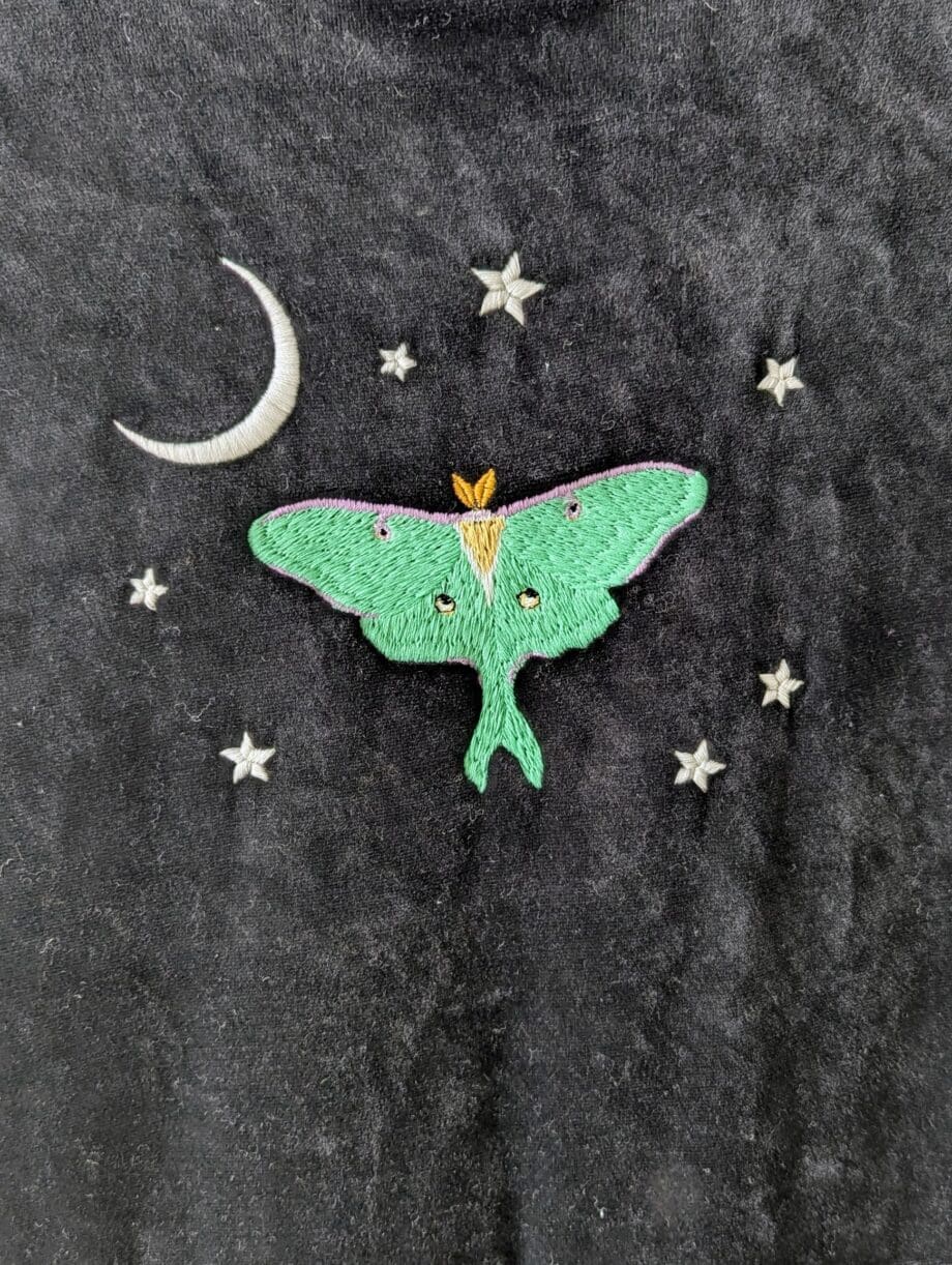 Detail of the embroidery on back of dress. Mint green luna moth with a white crescent moon in the top left of the design, surrounded by seven tiny white stars.