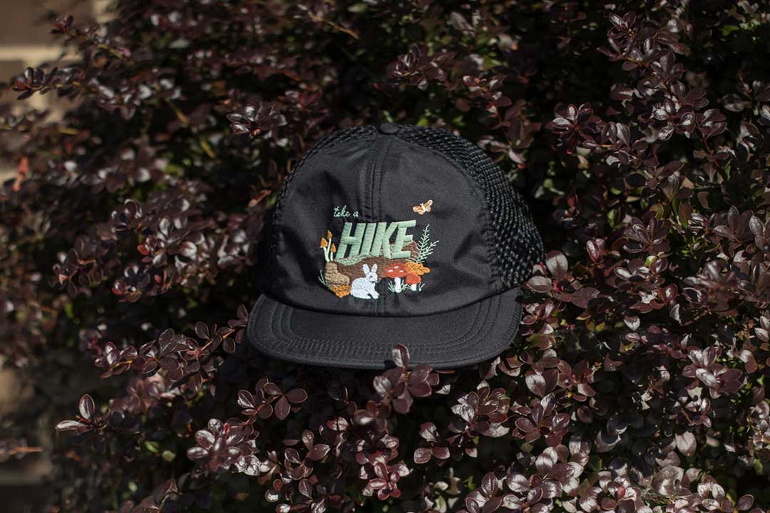 meshback trail cap with cute nature scene embroidery that says "take a hike" by Crewel & Unusual